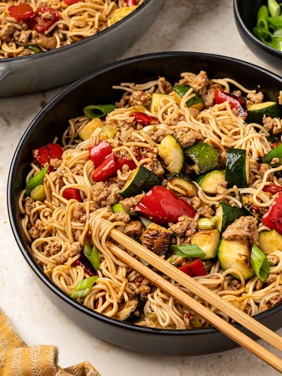 Side view of ground chicken and zucchini ramen stir-fry served in black bowl with chopsticks.