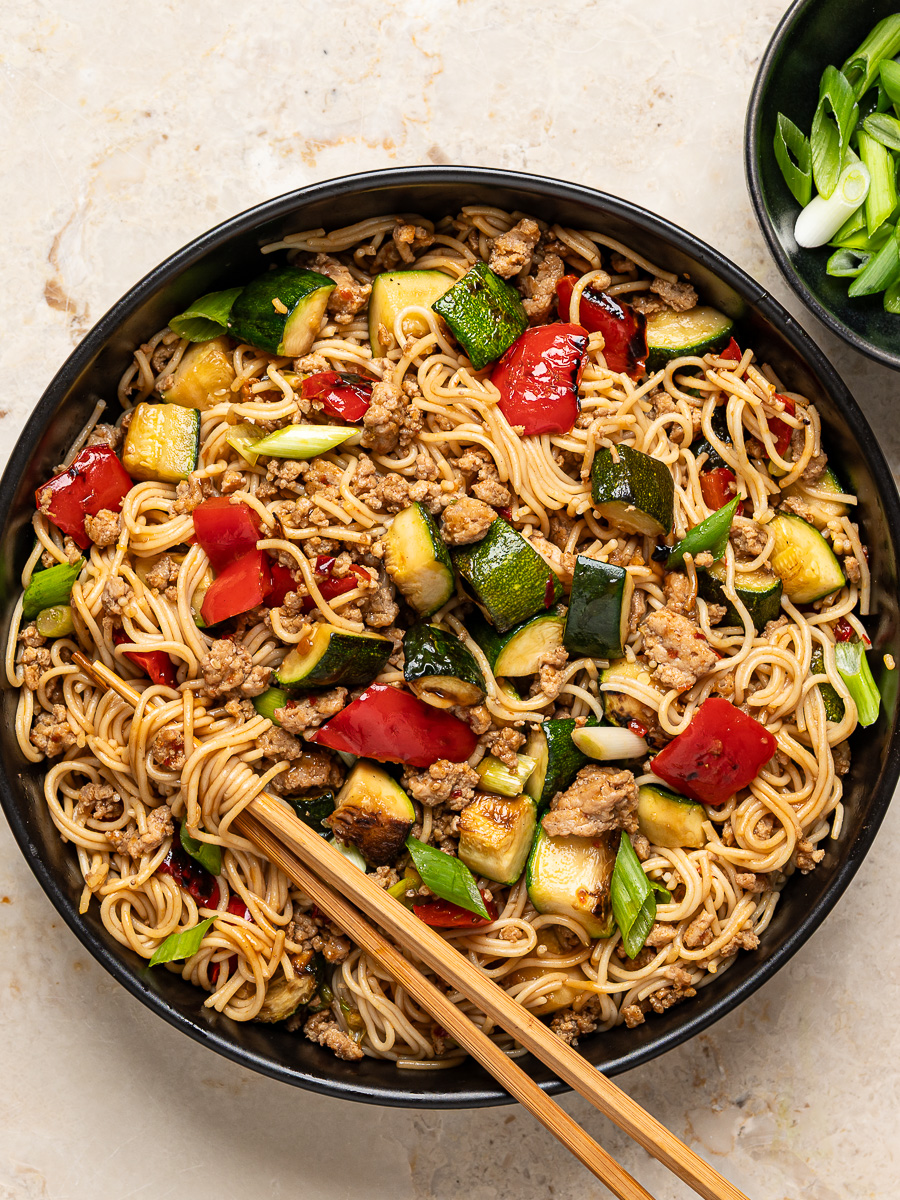 Ground chicken and zucchini ramen stir-fry served in black bowl with chopsticks.