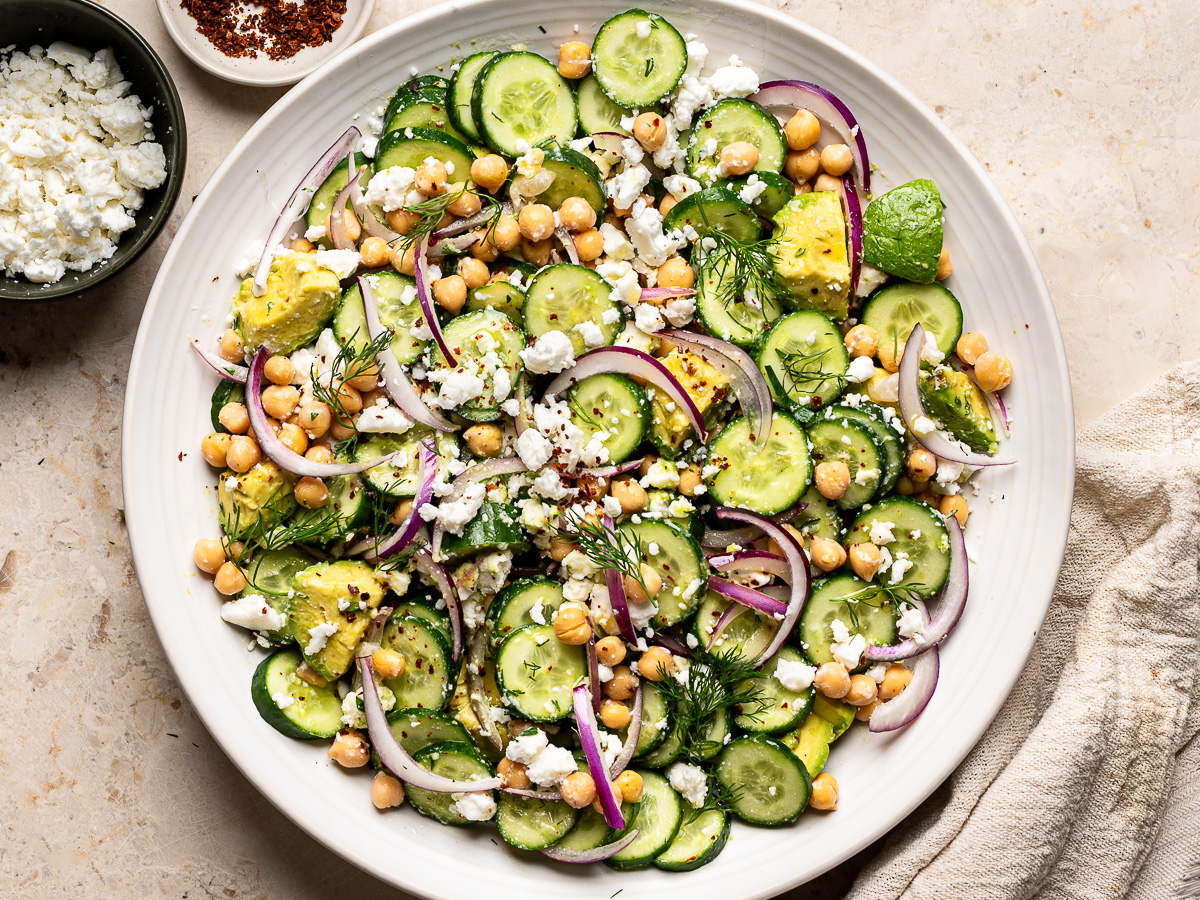 Cucumber avocado salad mixd in bowl with feta and dressing.