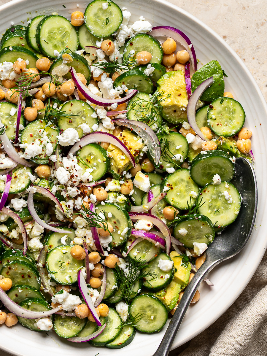Close up of Cucumber Avocado Salad topped with feta and fresh herbs served on a large white serving bowl.