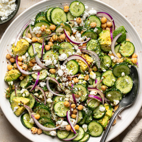 Cucumber Avocado Salad topped with feta and fresh herbs served on a large white serving bowl.