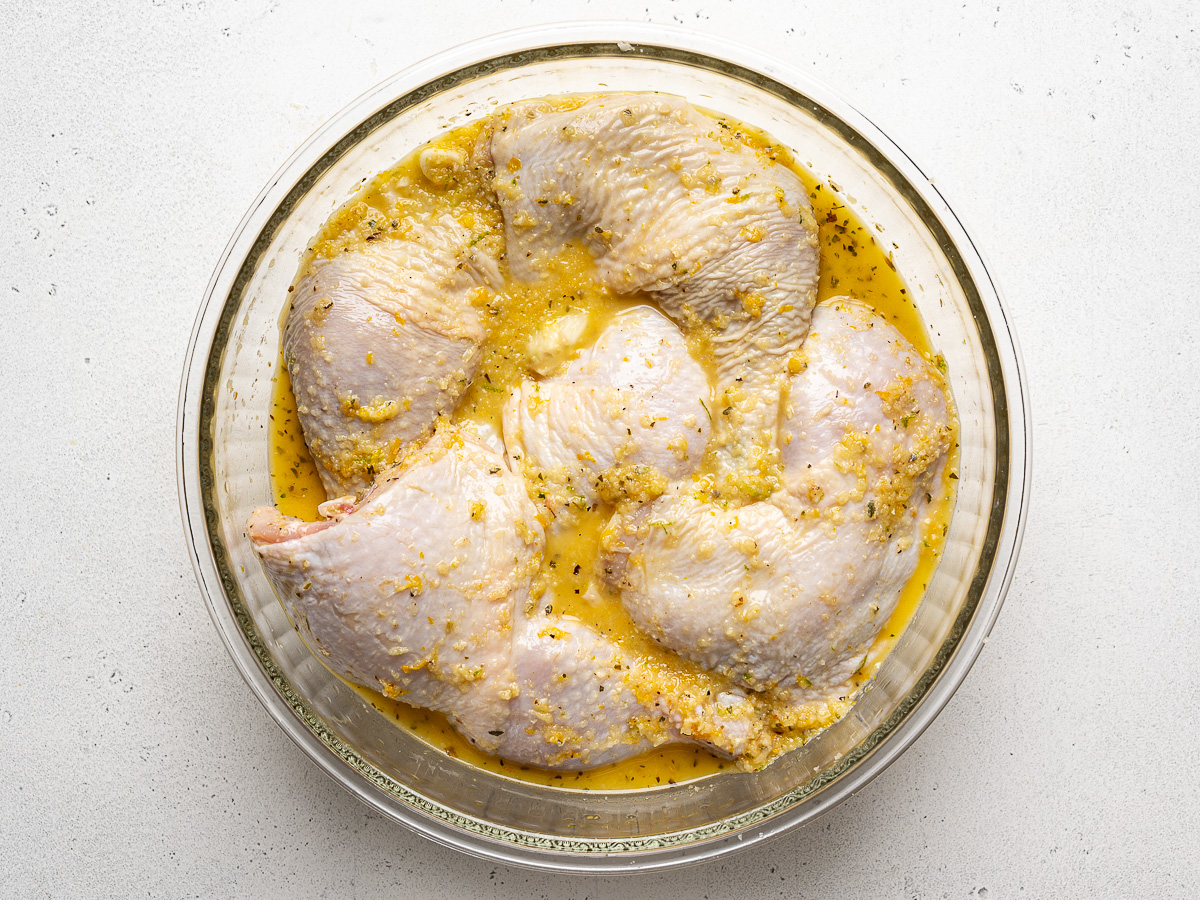 Chicken legs marinating in mojo marinade in glass bowl.