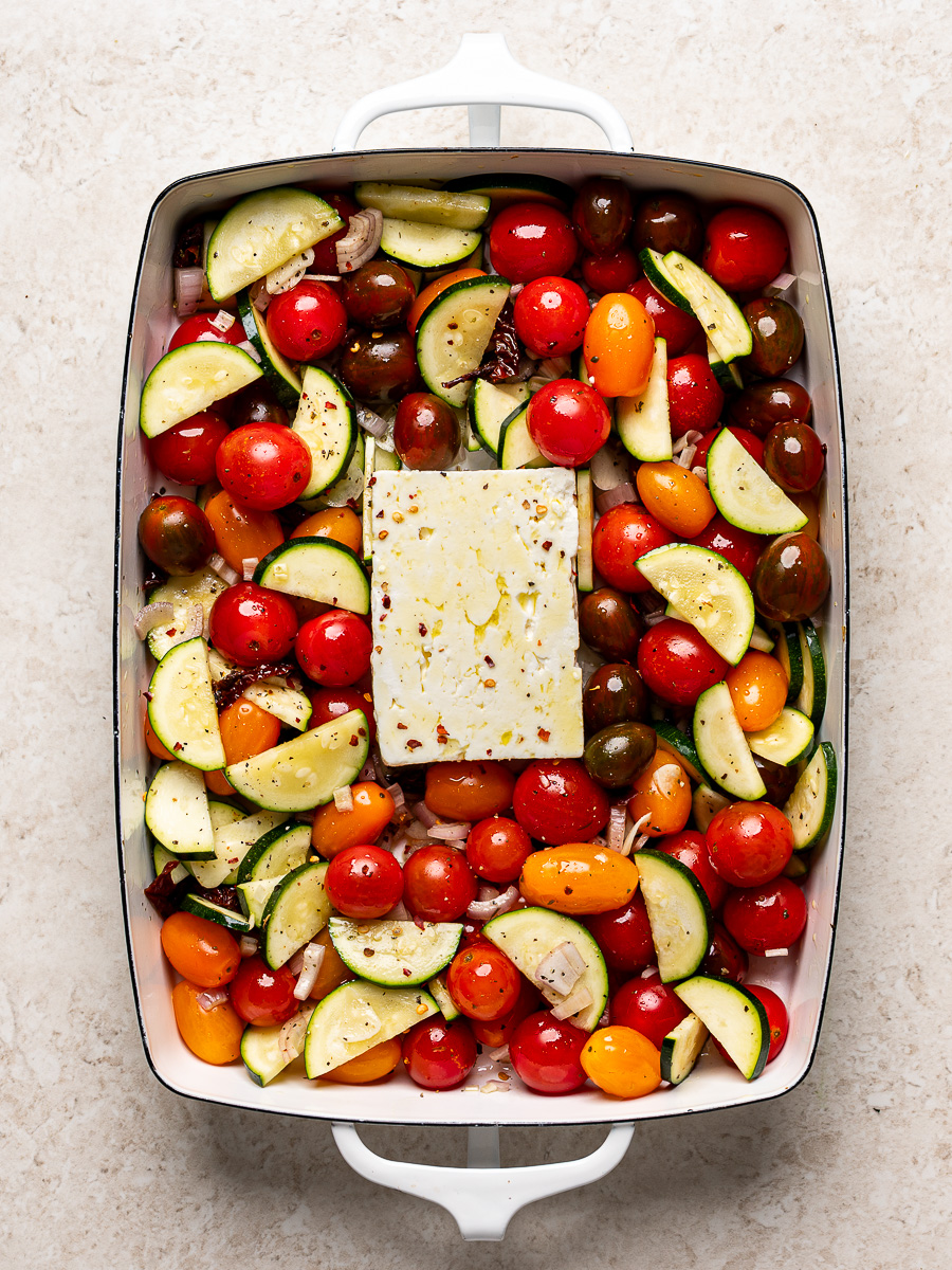 A block of feta nestled in middle of the baking dish with the cherry tomatoes and veggies.