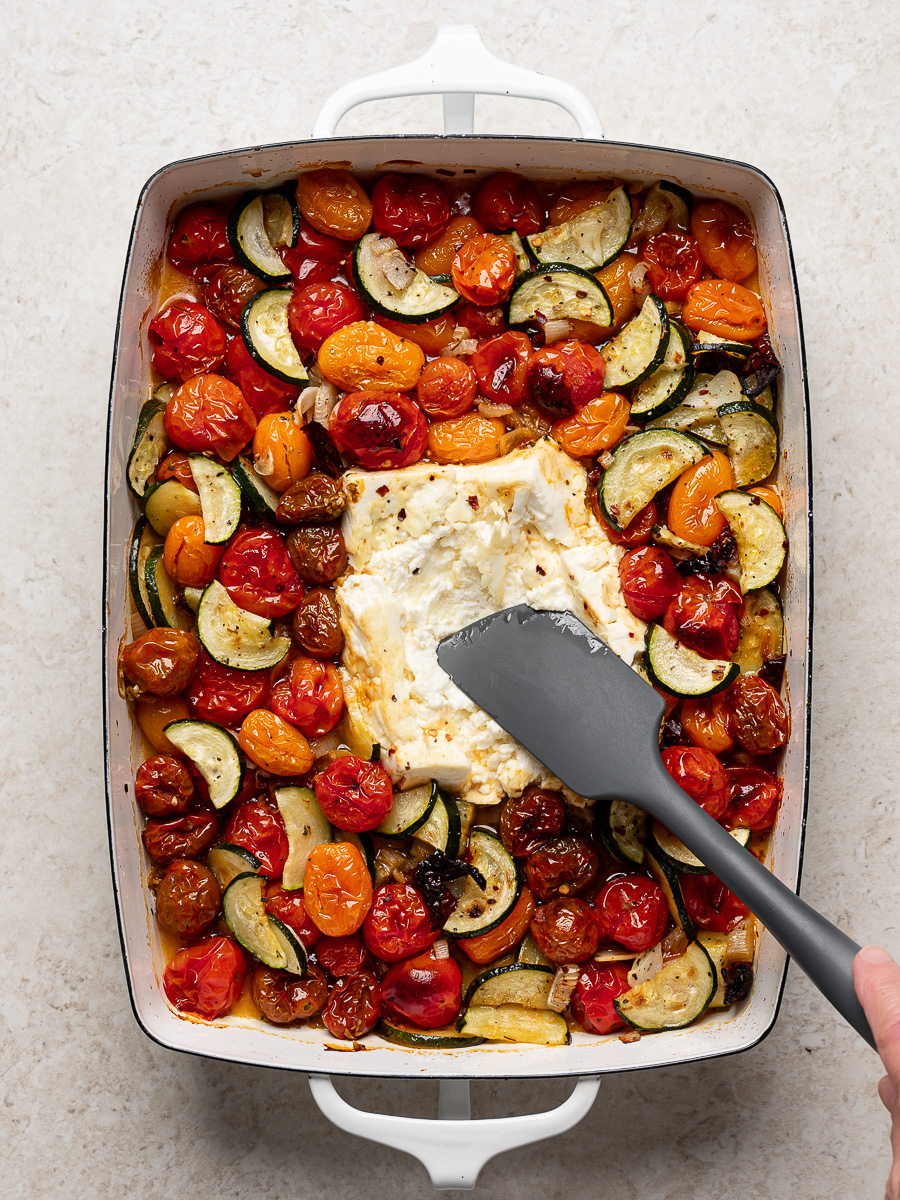 Mashing the block of baked feta with a spatula right in the baking dish.