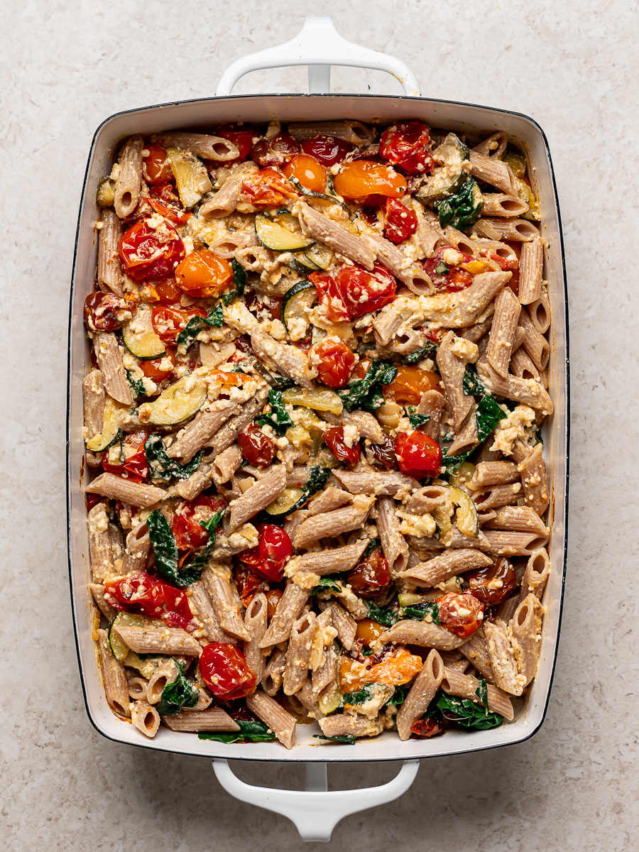 Cooked penne pasta and kale mixed in with the baked feta and vegetable mixture in baking dish.