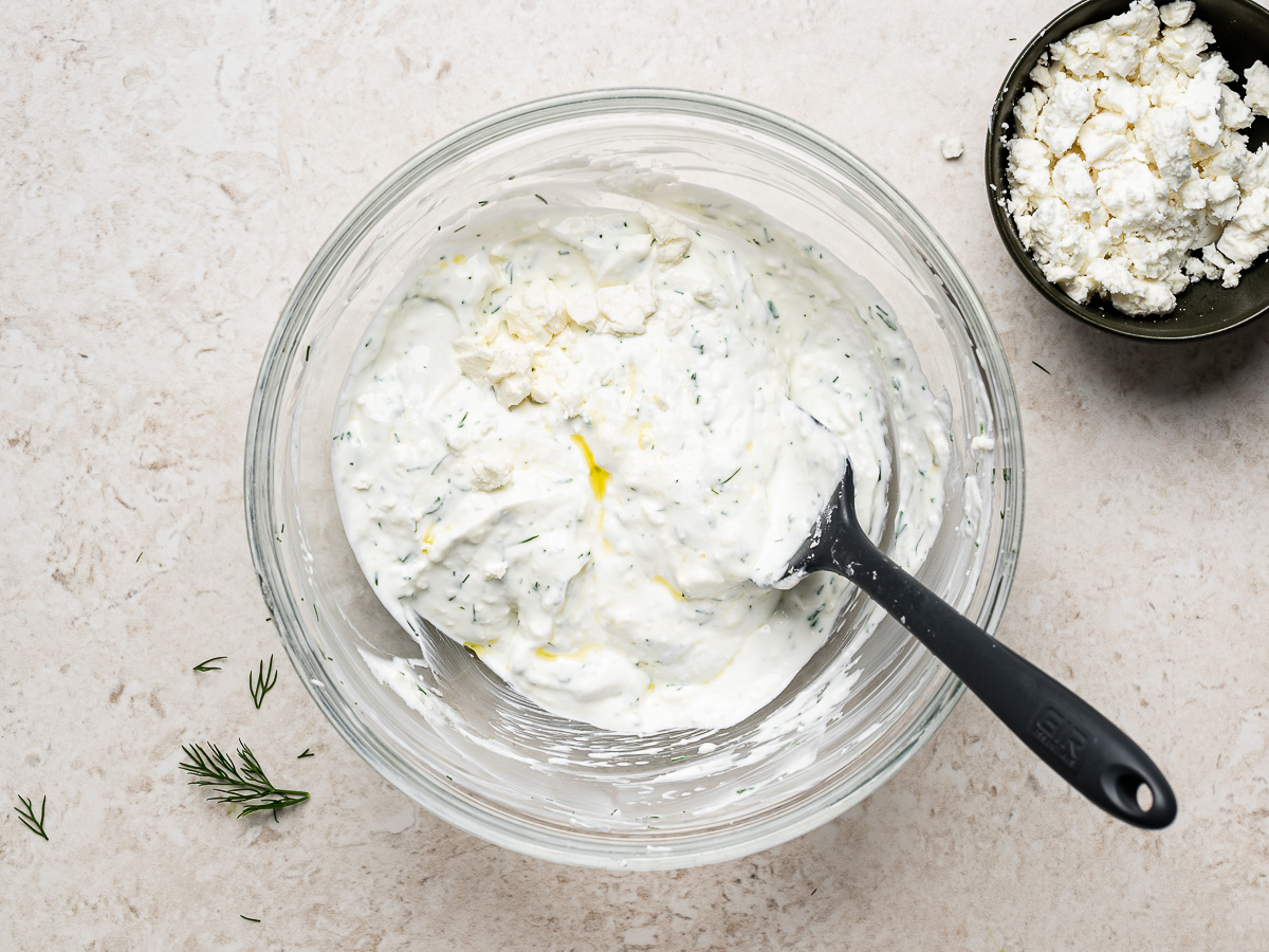 Greek yogurt, feta, dill, lemon juice, garlic, and seasonings being combined in a glass bowl to make the feta yogurt sauce.