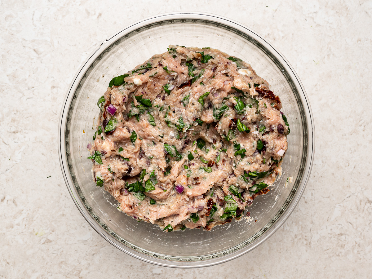 Ground chicken, vegetables, herbs, and seasonings combined in a glass bowl.