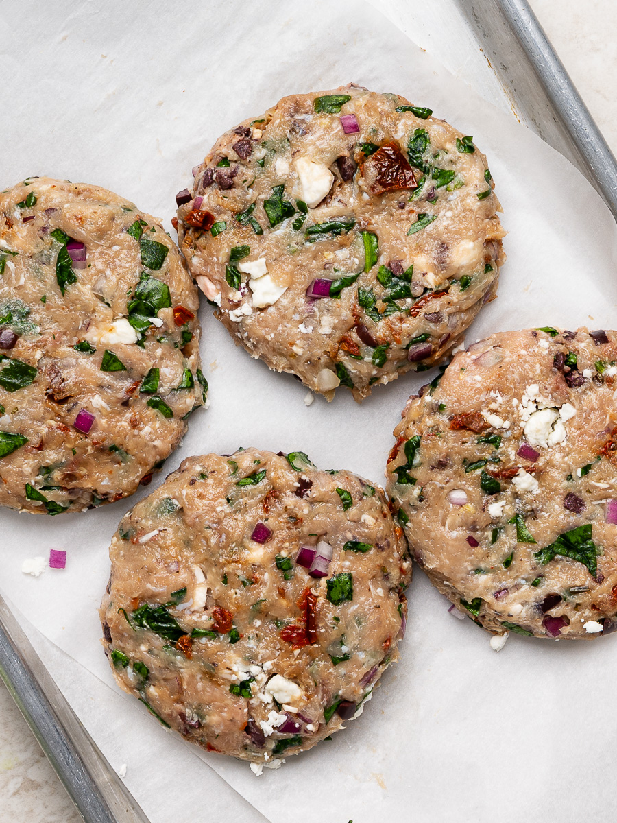 Four uncooked chicken burger patties arranged on a small baking sheet.