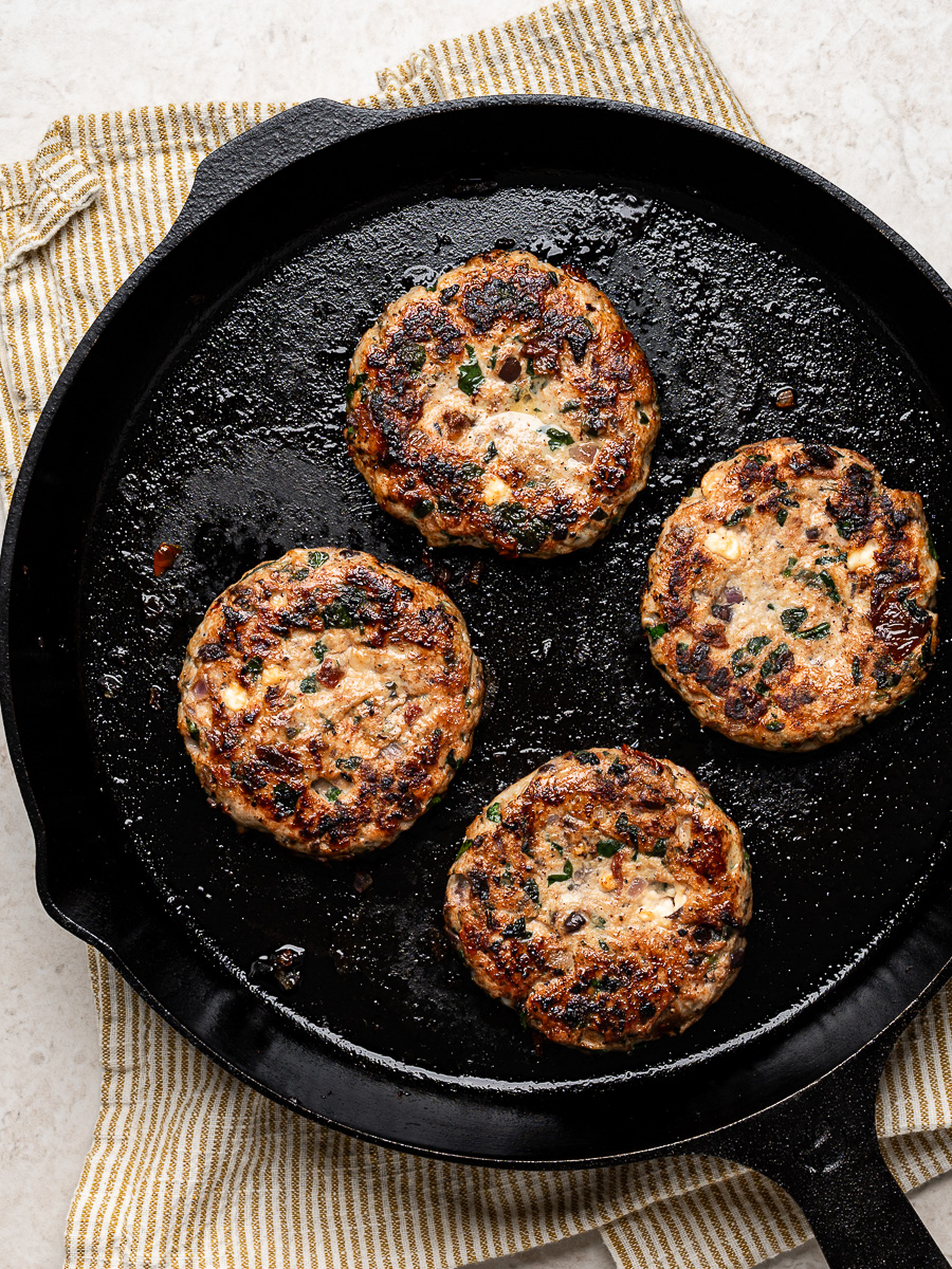Four cooked chicken burger patties arranged in a cast iron skillet.