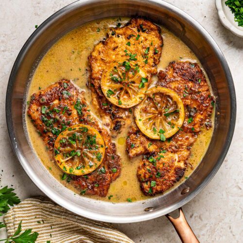 Golden Chicken Francese cutlets with lemon butter sauce, lemon slices, and fresh parsley served in a Lagostina skillet.