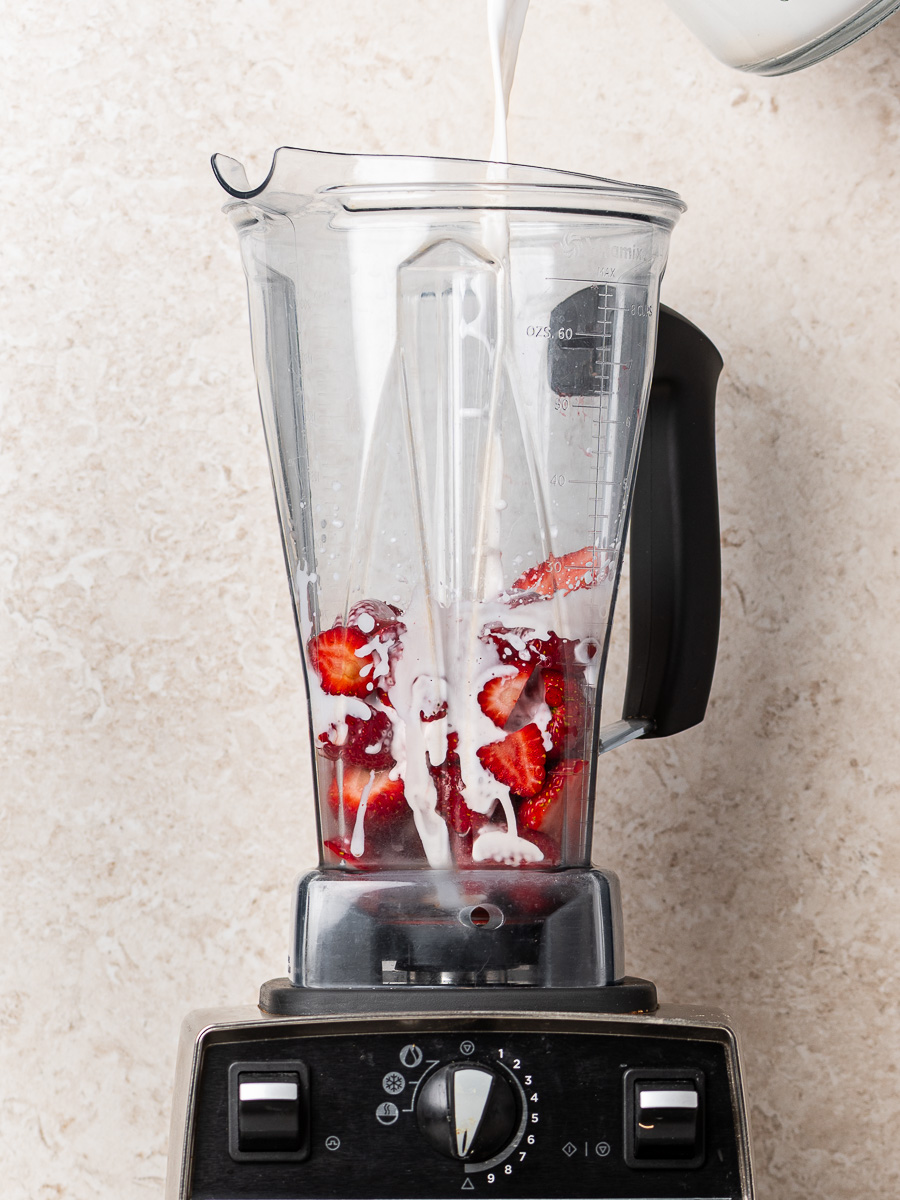 Fresh strawberries in a blender as milk is poured over them to make the base for strawberries and cream chia pudding.