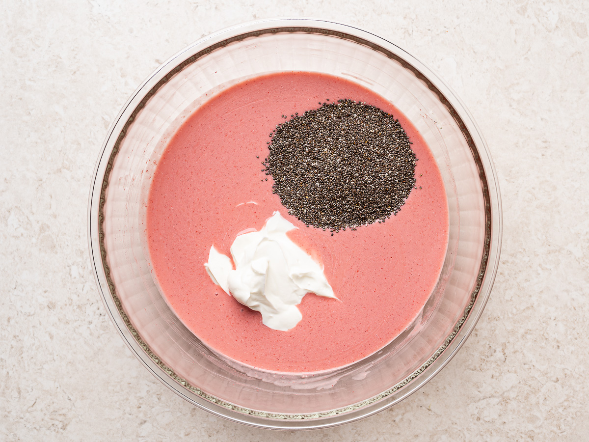 Strawberry and milk mixture in a glass bowl with Greek yogurt and chia seeds added, ready to be whisked together.