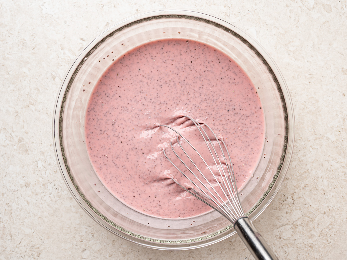 Strawberry chia pudding mixture being whisked in a glass bowl to combine the yogurt and chia seeds.