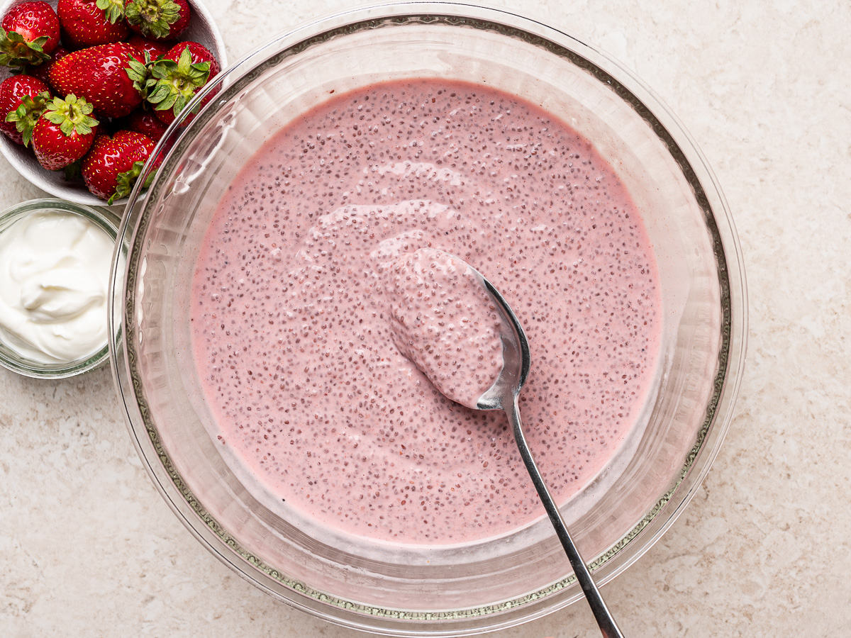 Chilled strawberries and cream chia pudding in a glass bowl with a spoon scooping up a creamy spoonful.