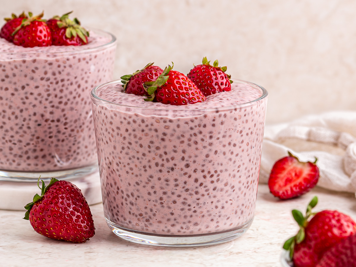 Two glass containers of strawberries and cream chia pudding topped with fresh strawberries.