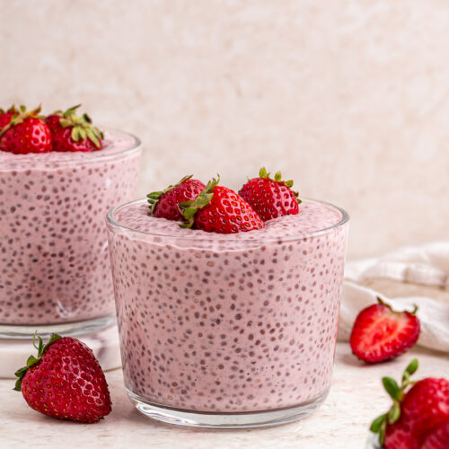 Two glass containers of strawberries and cream chia pudding topped with fresh strawberries.