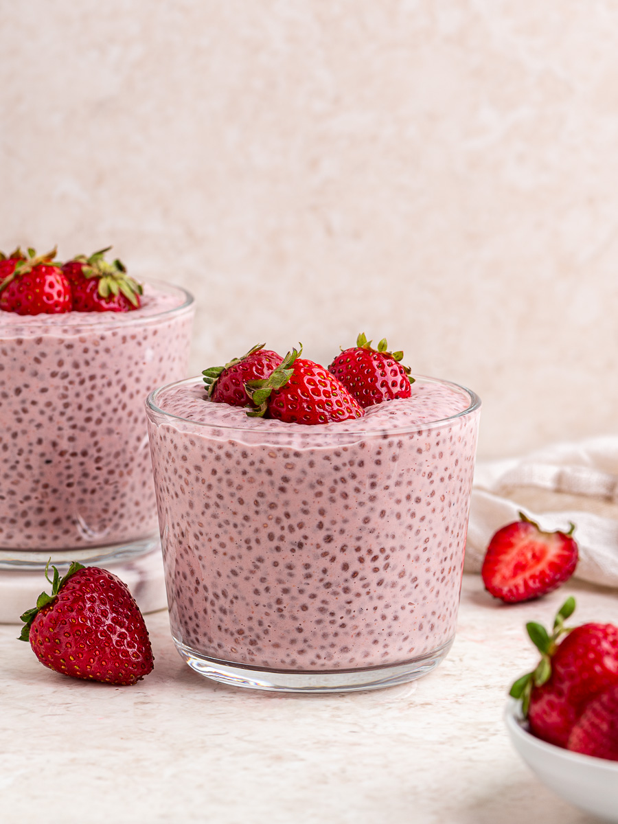Two glass containers of strawberries and cream chia pudding topped with fresh strawberries.