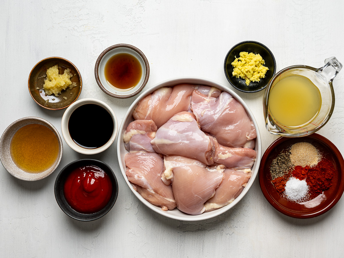 Ingredients for Huli Huli chicken arranged in individual bowls, including pineapple juice, soy sauce, ketchup, honey, ginger, garlic, and spices.
