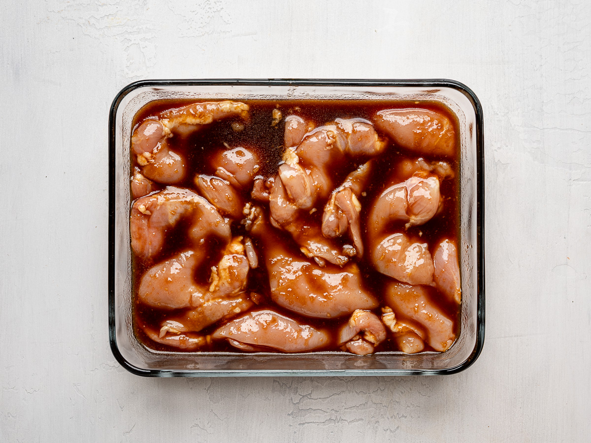 Boneless, skinless chicken thighs marinating in a pineapple-soy marinade in a glass baking dish.