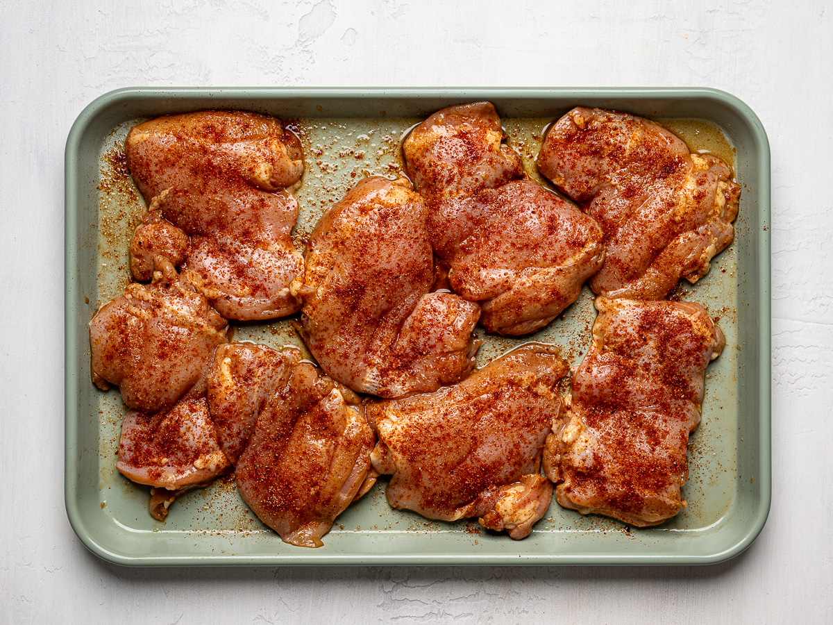 Boneless, skinless chicken thighs coated with dry rub and arranged on a parchment-lined sheet pan, ready for grilling.