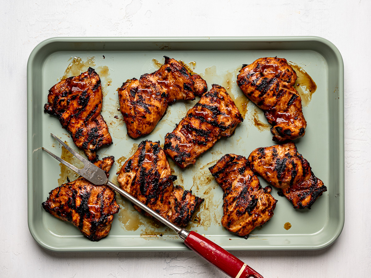 Grilled Huli Huli chicken thighs arranged on a sheet pan, showing caramelized and lightly charred edges.