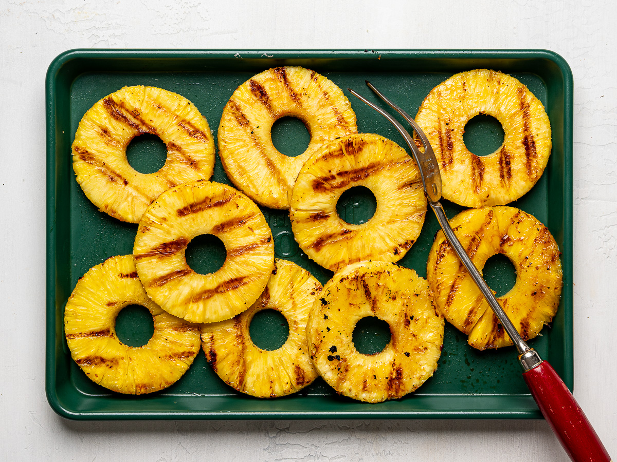 Pineapple rings with grill marks arranged on a sheet pan after grilling.