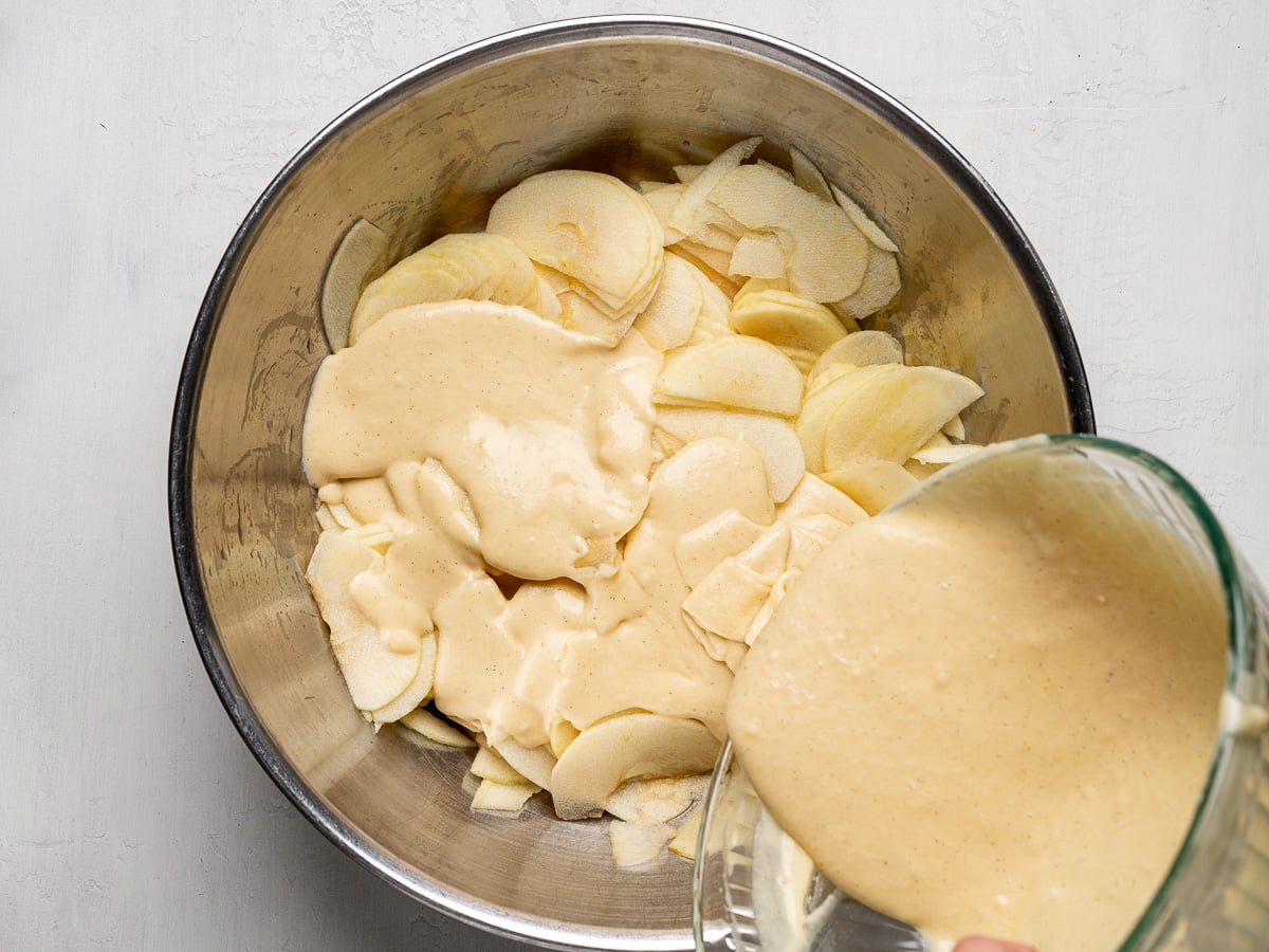 Pouring batter over sliced apples in mixing bowl.