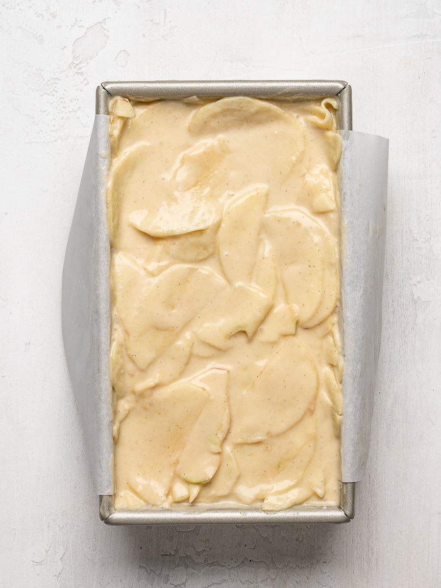 Apple slices that have been coated in batter layered tightly in loaf pan.