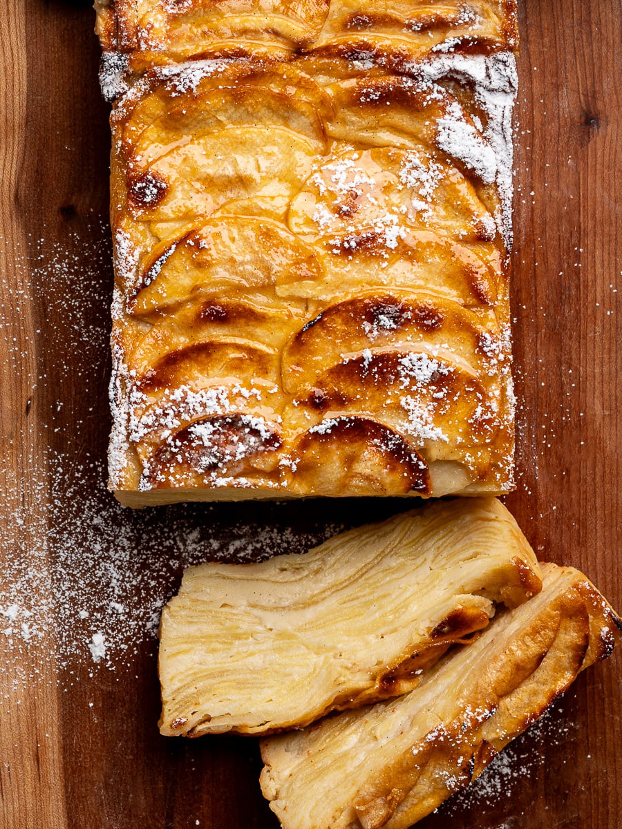 Top view of invisible apple cake sprinkled with powdered sugar with two slices of cake on the side.
