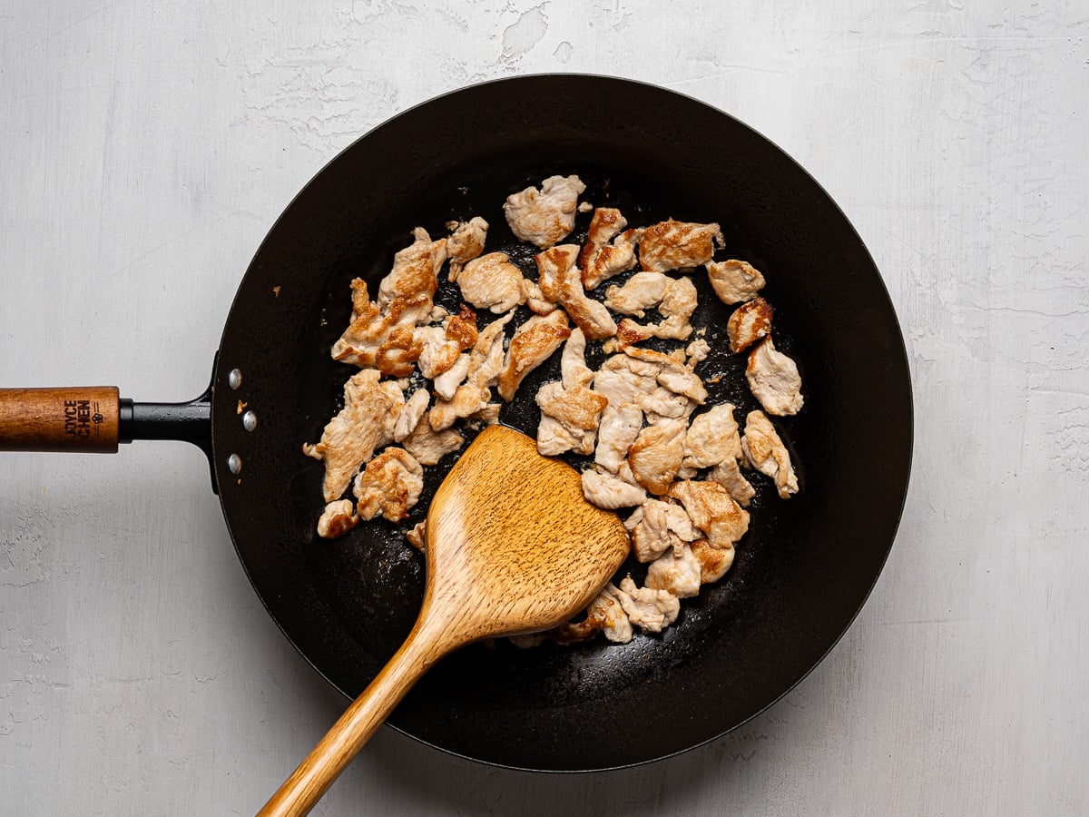 Cooked thinly sliced chicken pieces in wok.