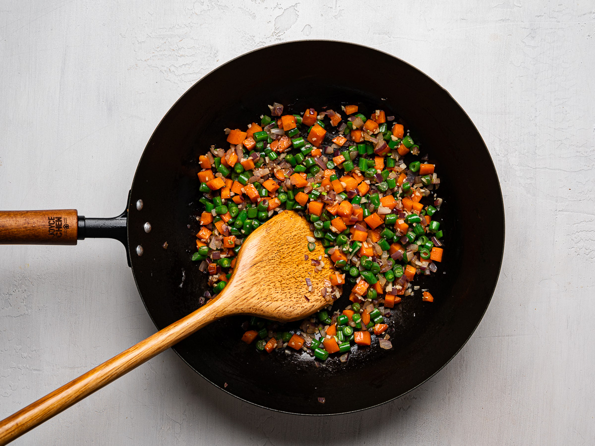 Finely diced onion, carrots, and green beans stir-fried in wok.