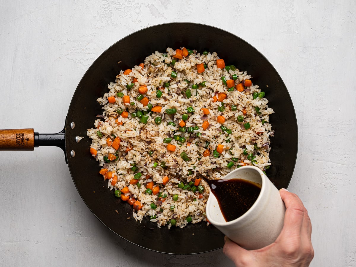 Pouring sauce over stir-fried rice and veggies.