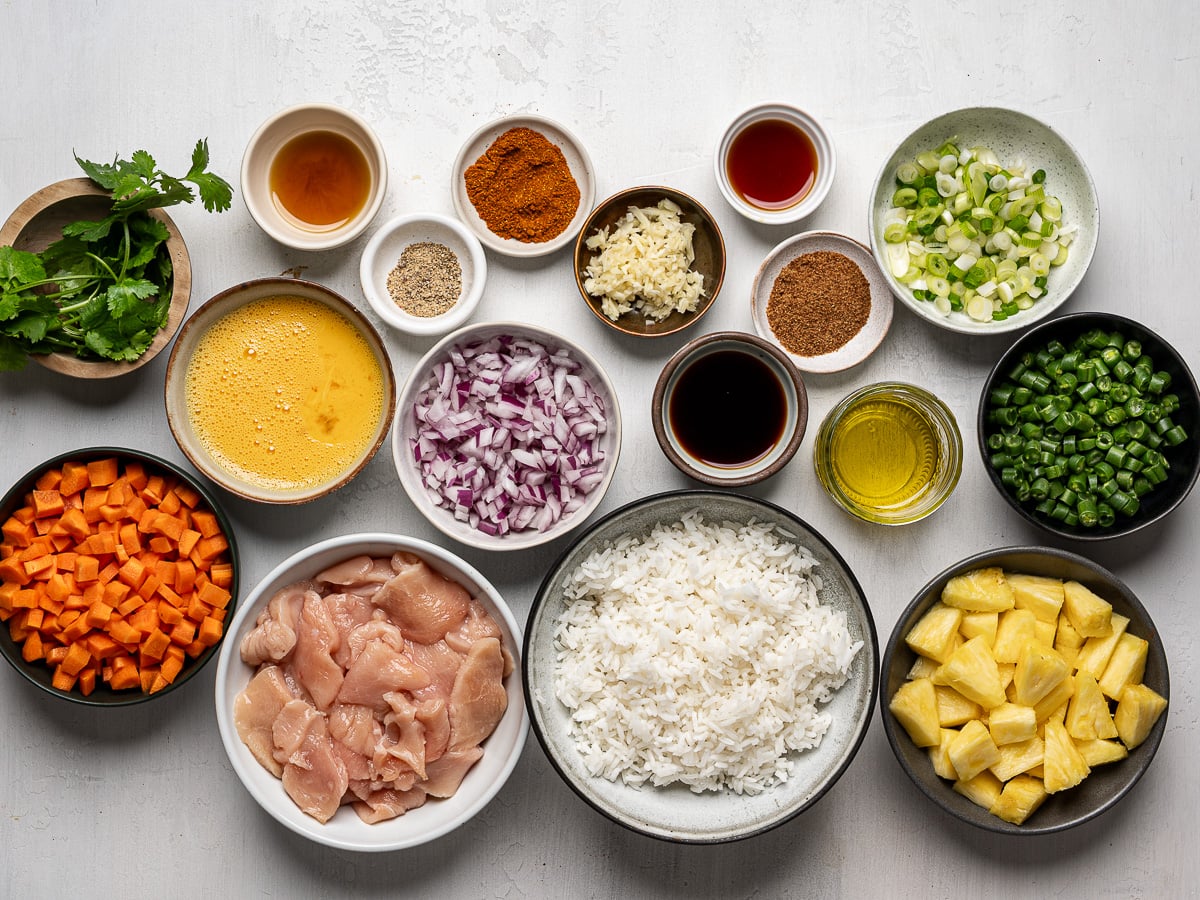 Ingredients for fried rice prepared in bowls including diced pineapple, sliced raw chicken, chopped veggies, and aromatics.