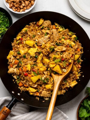 Pineapple fried rice with chicken in wok garnished with cilantro and green onions.